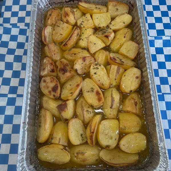 Roasted potatoes with herbs in a foil pan, sitting on a blue and white checkered tablecloth.