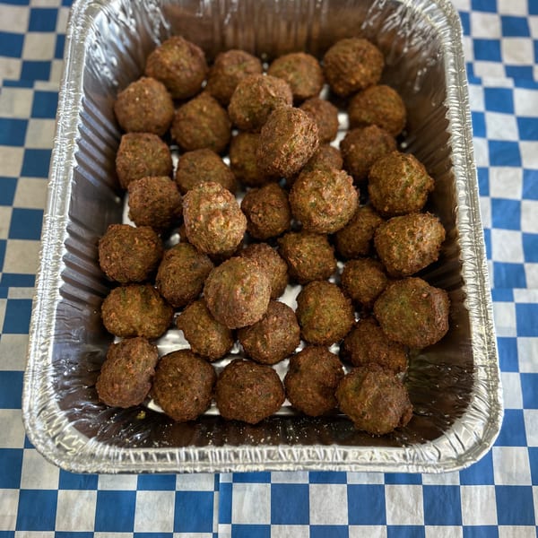 A foil pan filled with dozens of golden-brown falafel sits on a blue and white checkered tablecloth.