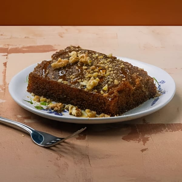 A slice of Greek walnut cake, karidopita, drizzled with syrup and topped with walnuts on a white plate.