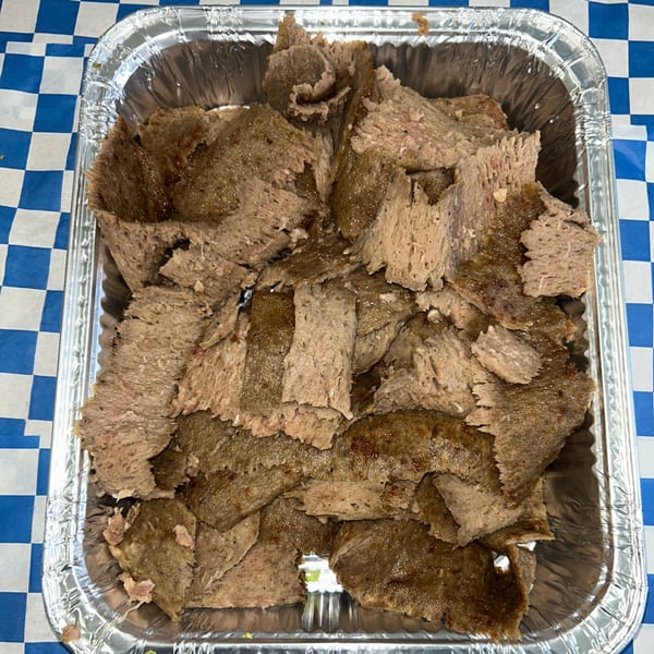 Shaved gyro meat in a foil tray, resting on a blue and white checkered tablecloth.