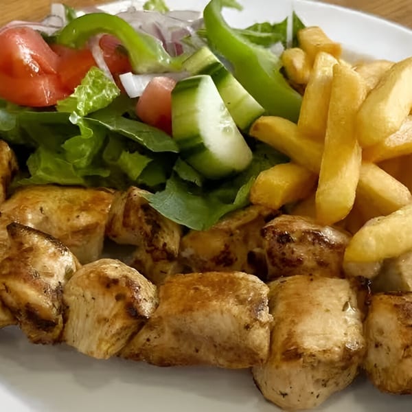 Grilled chicken souvlaki with golden fries and a fresh Greek salad on a white plate.