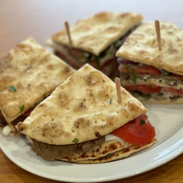 Four triangular Greek pita sandwiches with meat, tomatoes, and sauce, served on a white plate.