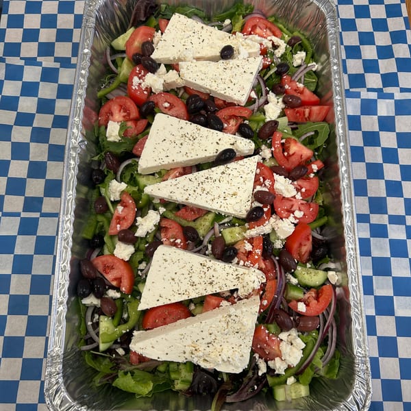 Large catering tray of Greek salad with lettuce, tomatoes, olives, and feta cheese.